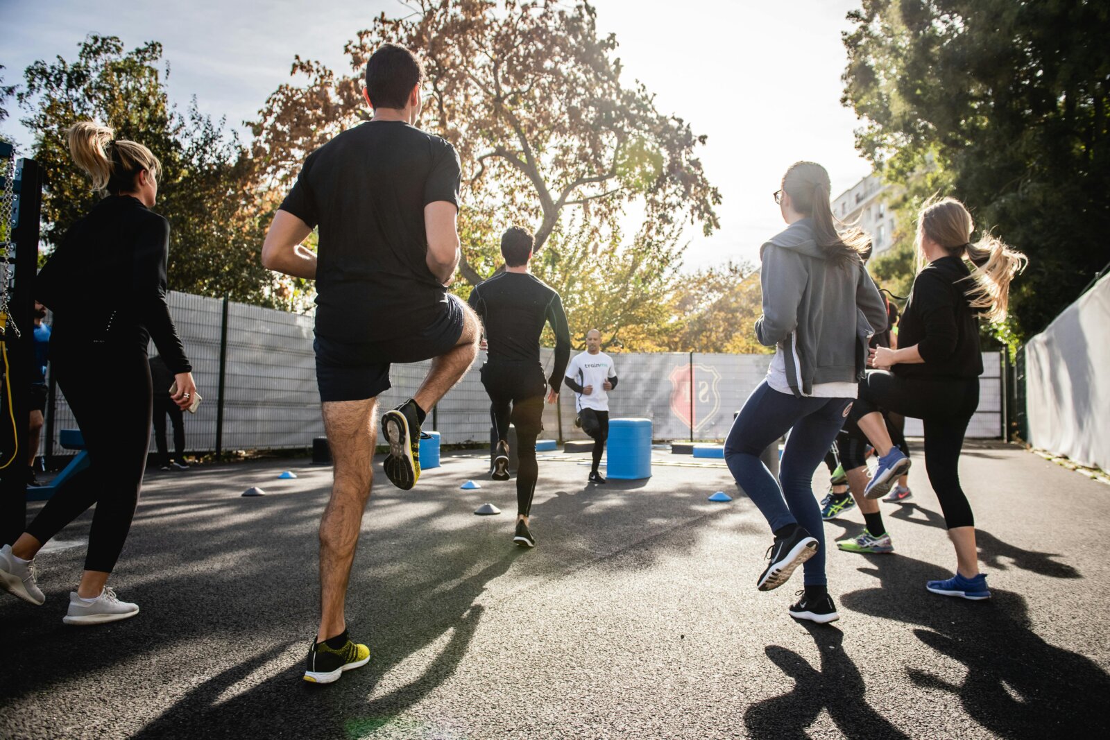 Group of people participating in outdoor fitness class, running and exercising together on pavement during golden hour sunlight